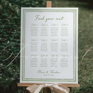 May include: A wedding seating plan displayed on a wooden easel. The white sign has a green border and features the words "Find your seat" at the top. Below are guest names organised by table number. The names are in a simple, elegant font.