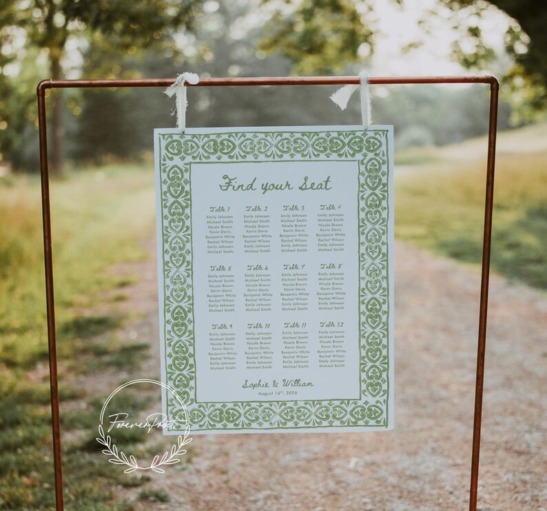 May include: A wedding seating chart with the text "Find your Seat" in elegant script. The chart features a green floral border and lists names under table numbers. The sign is suspended from a copper-colored metal frame.