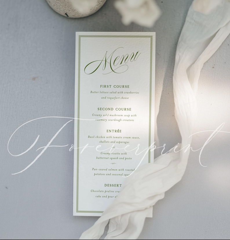 May include: A rectangular menu card with a green border and elegant script font. The menu lists courses like salad, soup, and entrees. A white fabric drapes across the image, adding a soft texture. The word "Menu" is at the top.
