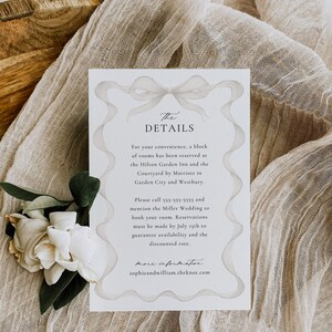 May include: A white card with a gray ribbon bow design. The text "The Details" is at the top of the card. The card provides information about hotel accommodations for a wedding. The text on the card includes the names of two hotels, phone number, and website address.