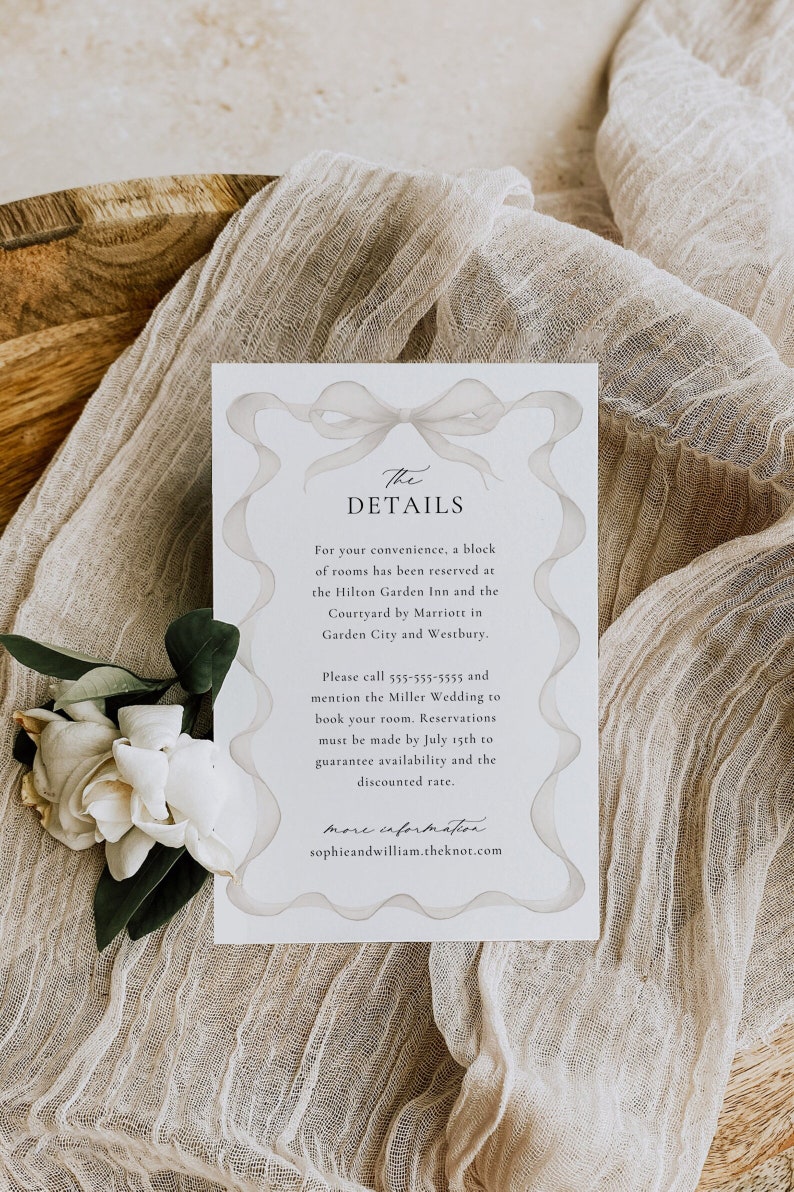 May include: A white card with a gray ribbon bow design. The text "The Details" is at the top of the card. The card provides information about hotel accommodations for a wedding. The text on the card includes the names of two hotels, phone number, and website address.