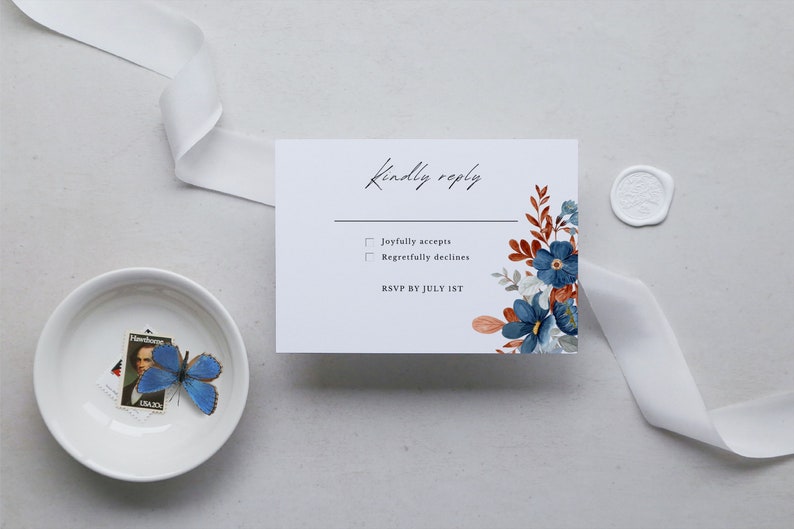 May include: A white RSVP card with floral accents in blue, rust, and gray, featuring the text "Kindly reply." A white ribbon and a small bowl with a blue butterfly and a stamp are also present.