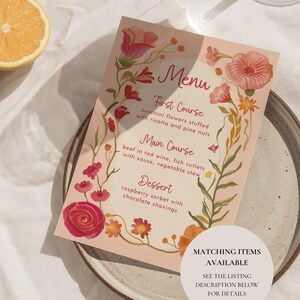 K&ouml;nnte beinhalten: Eine Men&uuml;karte mit floralem Design, mit rosa Hintergrund und einem dekorativen Rand aus rosa und orangefarbenen Blumen. Das Men&uuml; listet ein Drei-G&auml;nge-Men&uuml; auf: Zucchinibl&uuml;ten, Rindfleisch in Rotwein und Himbeersorbet. Ein runder Aufkleber sagt "Passende Artikel verf&uuml;gbar".