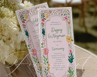 May include: Two pink wedding ceremony programs with floral borders and the text "Welcome to the wedding of Dagny & Neyman." The programs are on a wicker chair with a bouquet of white flowers.