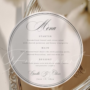 Op de afbeelding: Een ronde menukaart met een zwarte rand, met elegante scripttekst. Het menu bevat voorgerecht, hoofdgerecht en dessert. De kaart ligt op een zilveren schaal, met de menutekst "Menu" en de datum "15 juni 20xx".