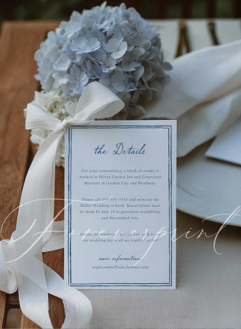 May include: A wedding details card with a blue border and text, next to a bouquet of blue and white flowers tied with a white ribbon. The card includes information about booking rooms and a phone number.