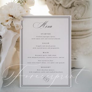 K&ouml;nnte beinhalten: Eine formelle Men&uuml;karte mit schwarzem Rand und eleganter Schriftart. Die Speisekarte umfasst Vorspeisen, Salat, Hauptgerichte wie Lammkoteletts und Seebarsch sowie Dessert. Wei&szlig;e Blumen und eine dekorative S&auml;ule befinden sich im Hintergrund.