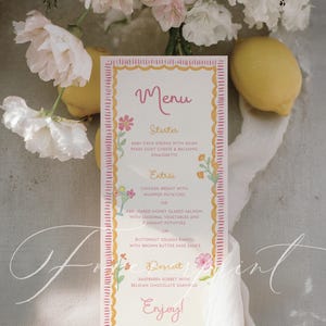 Pode incluir: Um cartão de menu decorativo com uma moldura floral rosa e amarela. O menu lista opções de entradas, pratos principais e sobremesas. O cartão é rodeado por flores brancas e limões.