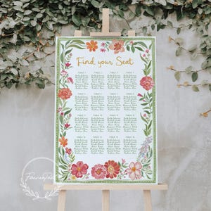 May include: A floral wedding seating chart on an easel. The sign features the words "Find your Seat" in gold script. The border is decorated with watercolor flowers in shades of pink, orange, and green. The names of the guests are listed under each table number.
