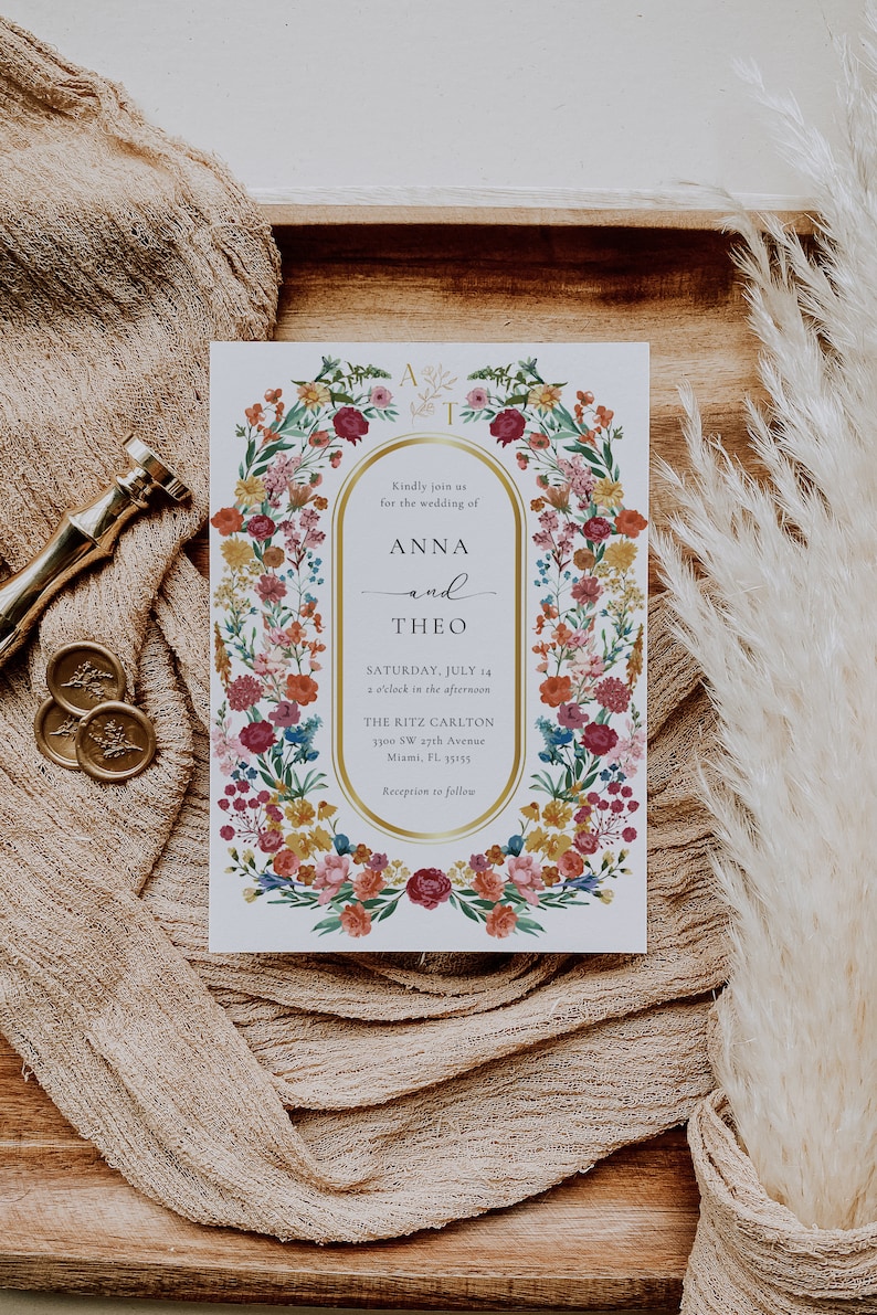 May include: A white wedding invitation with a gold border and floral design. The invitation reads "Kindly join us for the wedding of Anna and Theo, Saturday, July 14, 2 o'clock in the afternoon, The Ritz Carlton, 3300 SW 27th Avenue, Miami, FL 33155, Reception to follow."