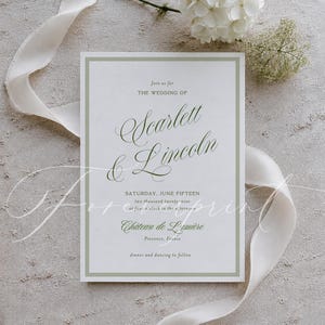 May include: A wedding invitation with the names "Scarlett & Lincoln" in elegant script. The invitation is white with a pale green border and text. A white ribbon and white flowers are arranged around the invitation.