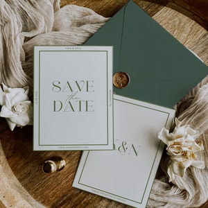 May include: Elegant wedding stationery set featuring a 'Save the Date' card with green accents, an envelope, and a wax seal. The card includes the text 'Save the Date' and the website address. Two gold rings and flowers are also present.