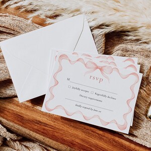 May include: RSVP card with a pink ribbon design. The card has a checkbox for "Joyfully accepts" and "Regretfully declines". It also includes a space for dietary requirements and asks for a response by June 1st.