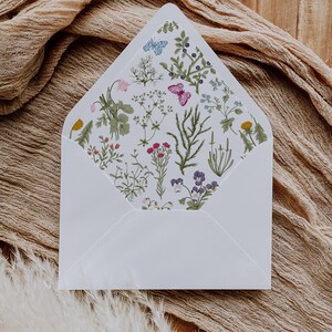 May include: A white envelope with a floral pattern on the inside flap. The pattern features a variety of flowers, leaves, and butterflies in shades of pink, blue, green, and yellow.