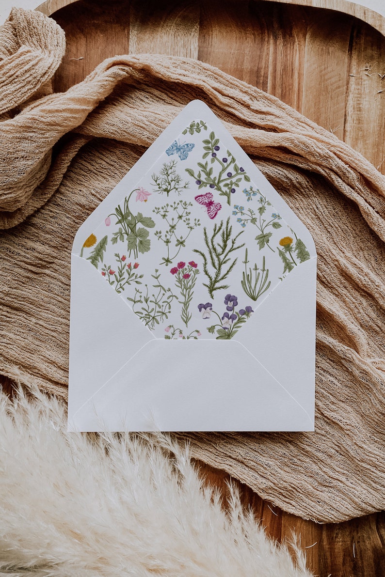 May include: A white envelope with a floral pattern on the inside flap. The pattern features a variety of flowers, leaves, and butterflies in shades of pink, blue, green, and yellow.