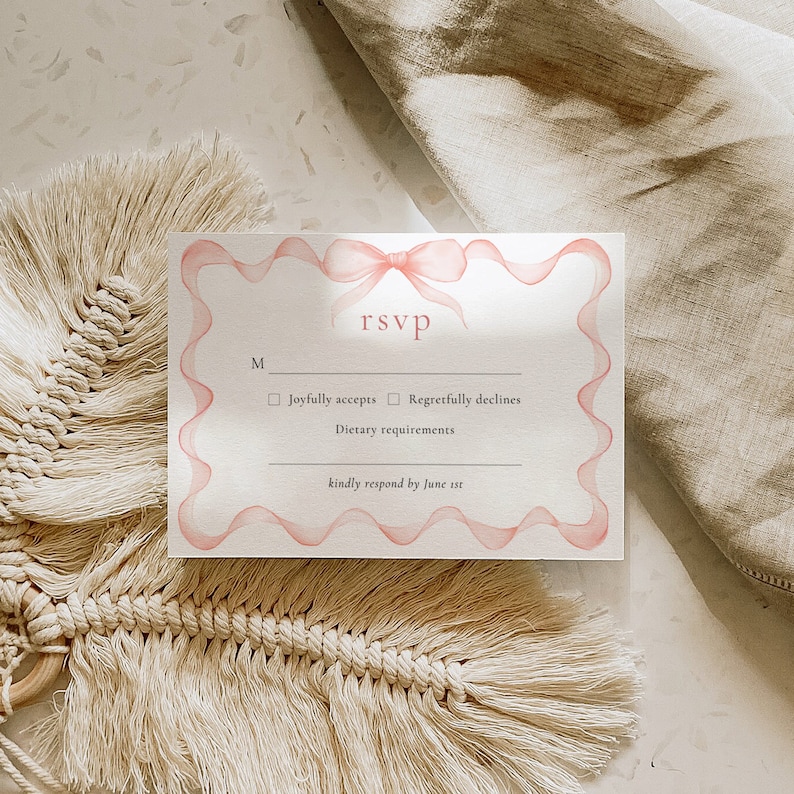 May include: A white RSVP card with a pink ribbon and bow design. The card has a section for guests to indicate whether they will joyfully accept or regretfully decline the invitation. It also includes a space for dietary requirements and a request to kindly respond by June 1st.