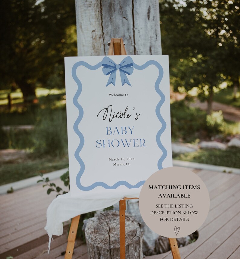 Peut inclure: Une pancarte blanche avec une bordure ondul&eacute;e bleue et un n&oelig;ud bleu sur le dessus. La pancarte indique "Bienvenue &agrave; la Baby Shower de Nicole" avec la date "15 mars 2024" et le lieu "Miami, FL". Un cercle brun avec du texte blanc indique "Articles assortis disponibles" et "Voir la description de la liste ci-dessous pour plus de d&eacute;tails".