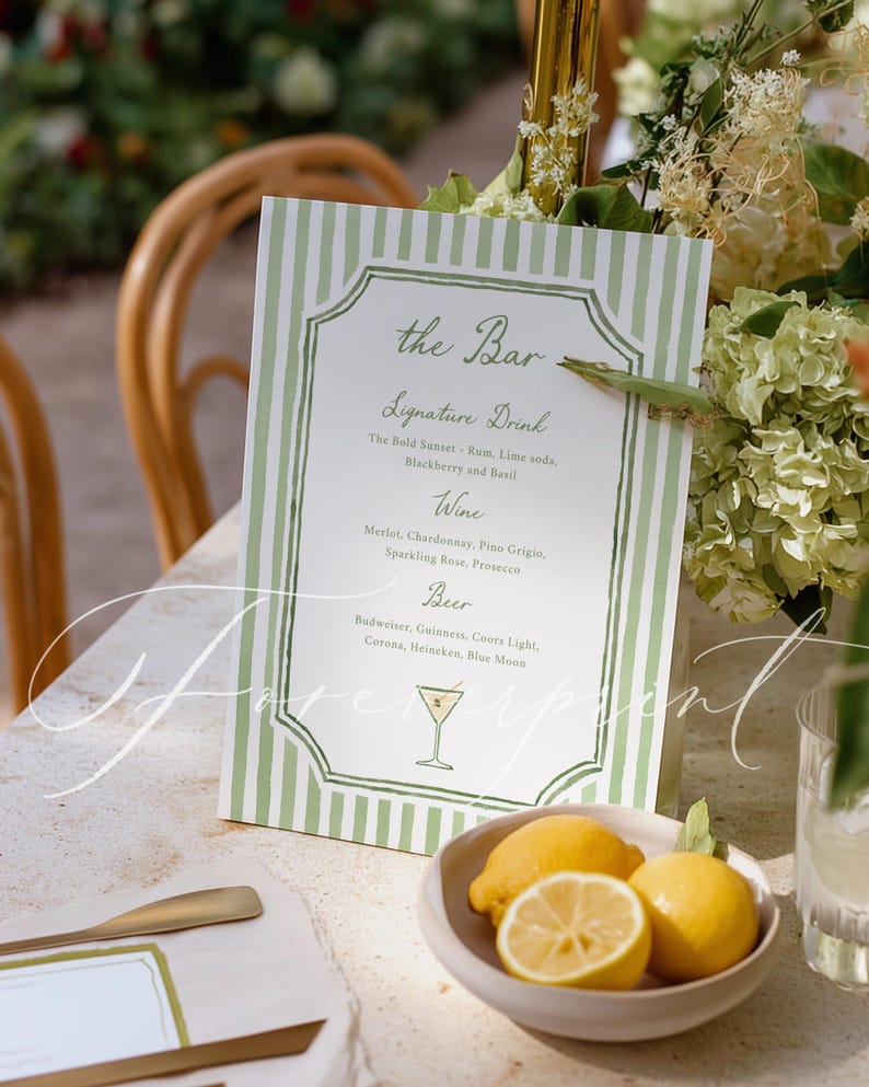 May include: A bar menu with a green and white striped design, featuring a list of signature drinks, wines, and beers. A small bowl of lemons sits in front of the menu. The menu is on a stone table.