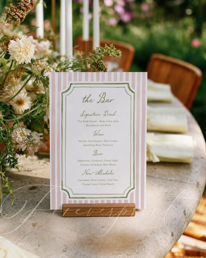 May include: A pink and white striped bar menu with a wooden base. The menu lists signature drinks, wines, beers, and non-alcoholic beverages. The text is in a decorative font with a green border.