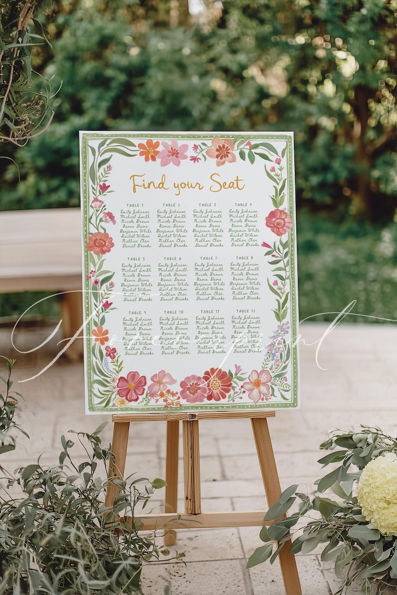 May include: A wooden easel displays a floral-decorated seating chart with the words "Find your Seat." The chart lists names under table numbers, surrounded by a border of pink, orange, and green flowers. The easel is set outdoors.