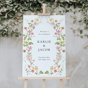 May include: A white wedding sign with a floral border. The sign reads "Welcome to the wedding of Karlie & Jacob, Cleveland, Ohio 14th August 20xx".
