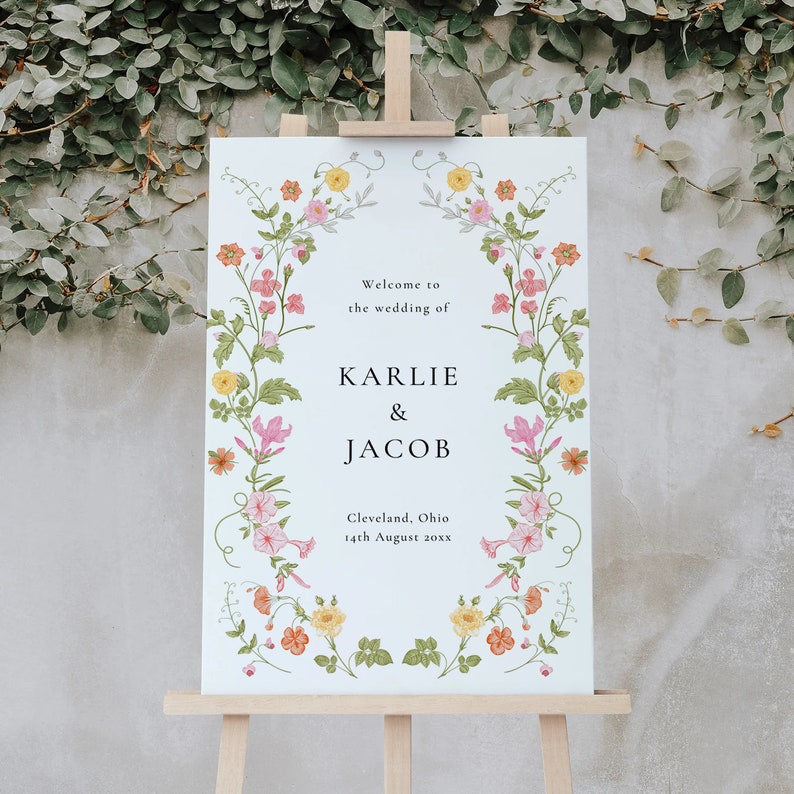 May include: A white wedding sign with a floral border. The sign reads "Welcome to the wedding of Karlie & Jacob, Cleveland, Ohio 14th August 20xx".
