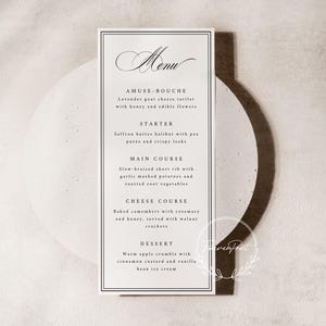 May include: A rectangular menu card with a black border and elegant script. The menu lists courses: Amuse-bouche, Starter, Main Course, Cheese Course, and Dessert. The menu items include detailed descriptions of the dishes.
