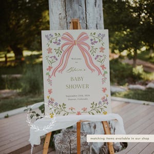 May include: A welcome sign for a baby shower with a pink bow and floral border. The sign reads "Welcome to Blaire's Baby Shower September 25th, 2026 Denver, Colorado".