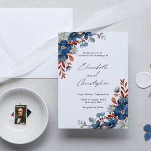 May include: Wedding invitation featuring blue floral watercolor design. The invitation includes the names "Elisabeth and Christopher", event details, and a white envelope. A white ribbon, a small bowl with a stamp, and a blue butterfly are also present.