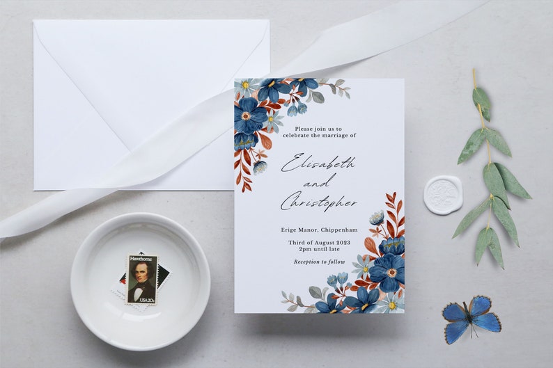 May include: Wedding invitation featuring blue floral watercolor design. The invitation includes the names "Elisabeth and Christopher", event details, and a white envelope. A white ribbon, a small bowl with a stamp, and a blue butterfly are also present.