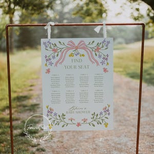 May include: A white seating chart with a floral design and pink ribbon. The chart has the text "Find Your Seat" and lists tables with names for a baby shower. The text "Blaize's Baby Shower" is at the bottom of the chart.