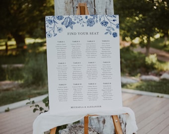 May include: A white seating chart with blue floral designs and the text "Find Your Seat". The chart lists tables with names of guests at each table. The bottom of the chart reads "Michaela & Alexander".