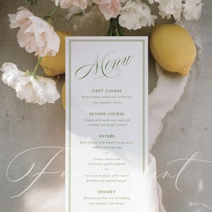 May include: A rectangular menu card with a green border and elegant script font. The menu lists courses like butter lettuce salad, creamy mushroom soup, basil chicken, and chocolate praline cake. Lemons and flowers are in the background.