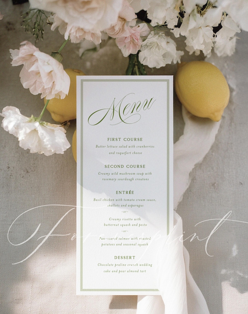 May include: A rectangular menu card with a green border and elegant script font. The menu lists courses like butter lettuce salad, creamy mushroom soup, basil chicken, and chocolate praline cake. Lemons and flowers are in the background.