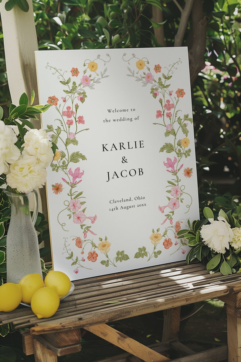 May include: A white wedding sign with a floral border. The sign reads "Welcome to the wedding of Karlie & Jacob, Cleveland, Ohio, 14th August 20xx".