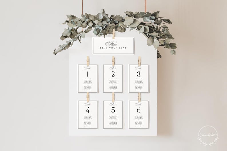 May include: A white seating chart with six table assignments, each held by a wooden clip. The top of the chart reads "Please Find Your Seat." Eucalyptus greenery and copper-colored wire hang above the chart.