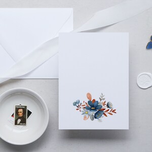 May include: A stationery set featuring a white envelope, card, and ribbon. The card is decorated with a floral design in shades of blue, orange, and gray. A small bowl holds a stamp, and a blue butterfly and wax seal are also present.