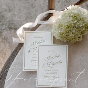 May include: Two wedding invitations with green text and borders, featuring the names "Scarlett & Lincoln" and event details. A white ribbon and a bouquet of white flowers are in the background. The text includes "Saturday, June Fifteen".