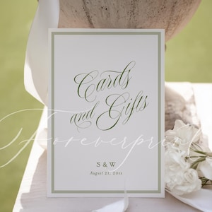 May include: A white sign with a green border and elegant script that reads "Cards and Gifts." The sign also includes the initials "S & W" and the date "August 21, 20xx." The sign is likely for a wedding or special event.