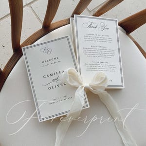 K&ouml;nnte beinhalten: Elegante Hochzeitskarten mit Willkommens- und Dankeskarten. Schwarzer Text auf wei&szlig;em Papier, gebunden mit einem cremefarbenen Band. Die Willkommenskarte zeigt die Namen "Camilla und Oliver" und das Hochzeitsdatum.