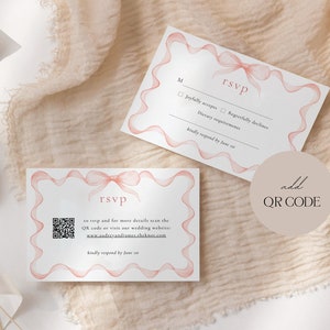 May include: A white RSVP card with a pink ribbon design. The card has a QR code and the text "to rsvp and for more details scan the QR code or visit our wedding website: www.audreyandjames.theknot.com kindly respond by June 1st".