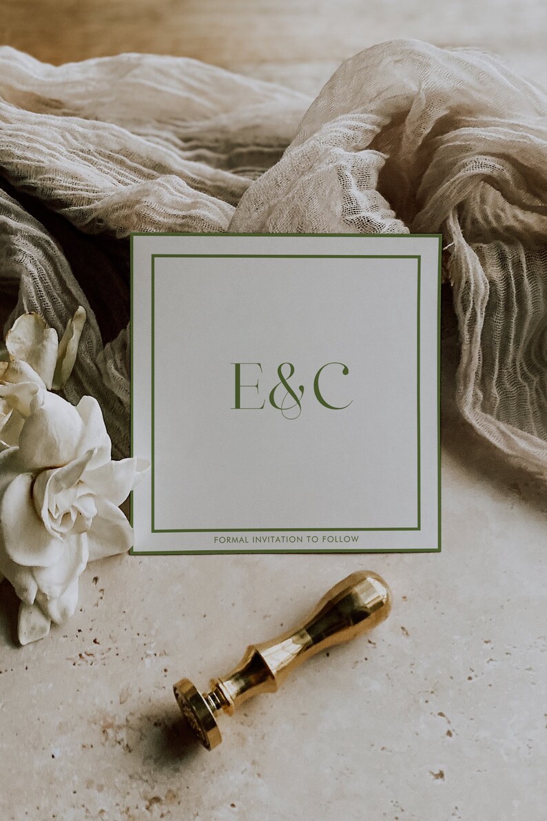 May include: A white card with a green border and the text "E&C" in a script font. Below the text is the phrase "Formal Invitation to Follow". The card is sitting on a beige surface with a white flower and a gold wax seal.