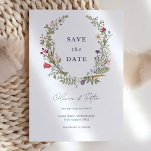 May include: Save the date card with a floral wreath design. The text reads "Save the Date" with the names "Olivia & Peter" and the wedding details: "are getting married!" "Lains Barn, Oxfordshire" "14th August 2022" "Invitation to follow"