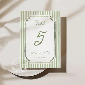 May include: A wedding table number card with a green and white striped border. The card features the word "Table" above the number "5" in a script font. Below the number are the names "Chloe & Nick" and the date "08.13.20xx".