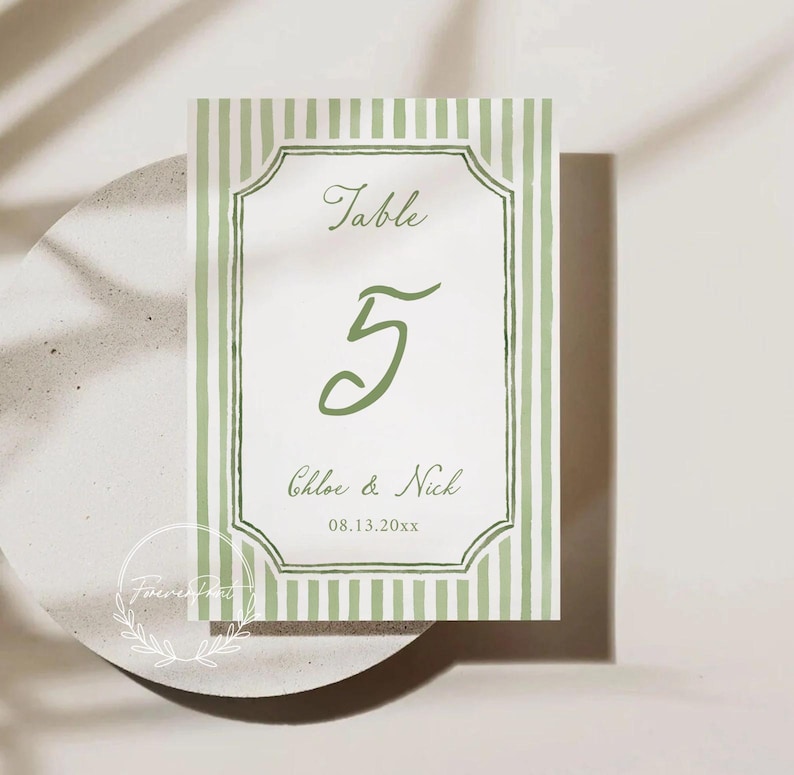 May include: A wedding table number card with a green and white striped border. The card features the word "Table" above the number "5" in a script font. Below the number are the names "Chloe & Nick" and the date "08.13.20xx".