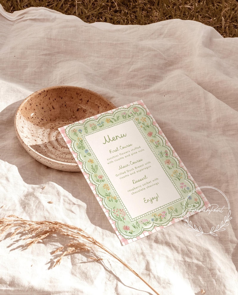 May include: A menu card with a floral border and a pink gingham background. The menu lists a first course of zucchini flowers, a main course of duck breast, and a dessert of raspberry sorbet. A speckled ceramic bowl is also in the image.