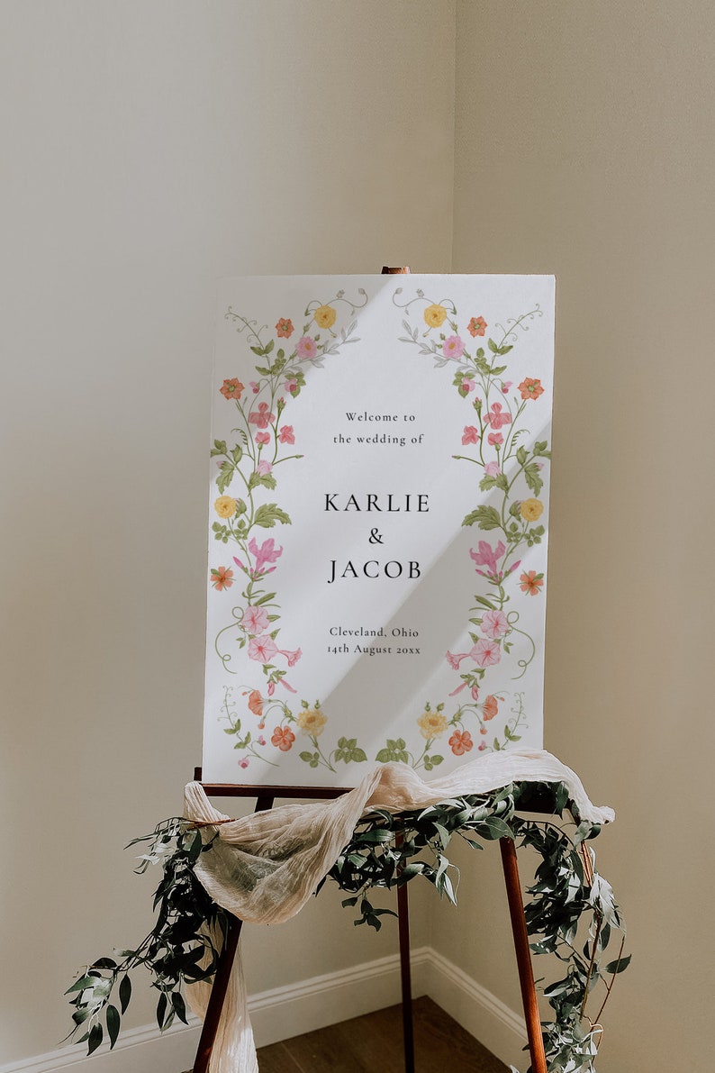 May include: A white wedding sign with a floral border. The sign reads "Welcome to the wedding of Karlie & Jacob, Cleveland, Ohio, 14th August 20xx".