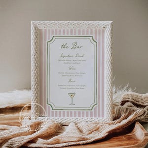 May include: A framed sign with a pink and white striped background and a decorative border. The sign reads "the Bar" and lists drink options: Signature Drink, Wine, and Beer. A cocktail illustration is at the bottom.