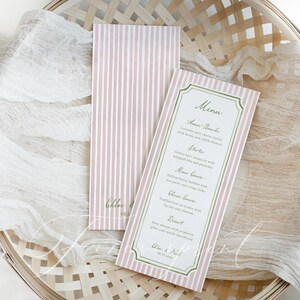 May include: Two pink and white striped menu cards with a decorative border. One card displays a menu with headings like "Amuse-Bouche" and "Starter." The menu includes text such as "Lavender goat cheese tartlets." The cards are on a woven basket.