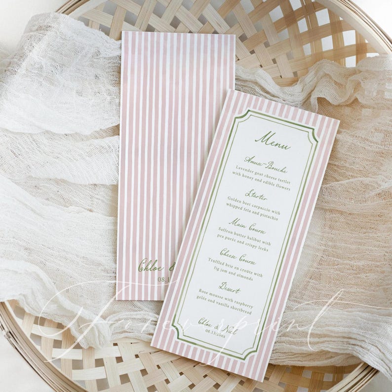May include: Two pink and white striped menu cards with a decorative border. One card displays a menu with headings like "Amuse-Bouche" and "Starter." The menu includes text such as "Lavender goat cheese tartlets." The cards are on a woven basket.